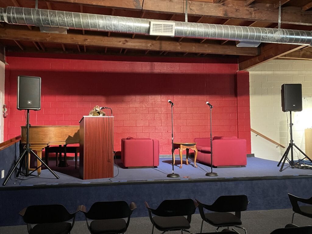 The stage of our event space, which includes a podium, microphones, and a bright, red wall.